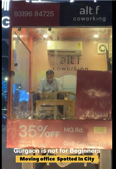 A man working inside a glass-walled truck converted into a mobile office in Gurgaon, equipped with a desk, chair, sofa, AC, and TV, going viral online.